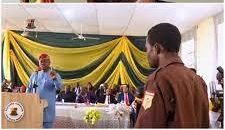 Governor Seyi Makinde standing beside a uniformed LAUTECH security guard during a public town hall meeting at the university campus, with staff and students listening attentively in the background.